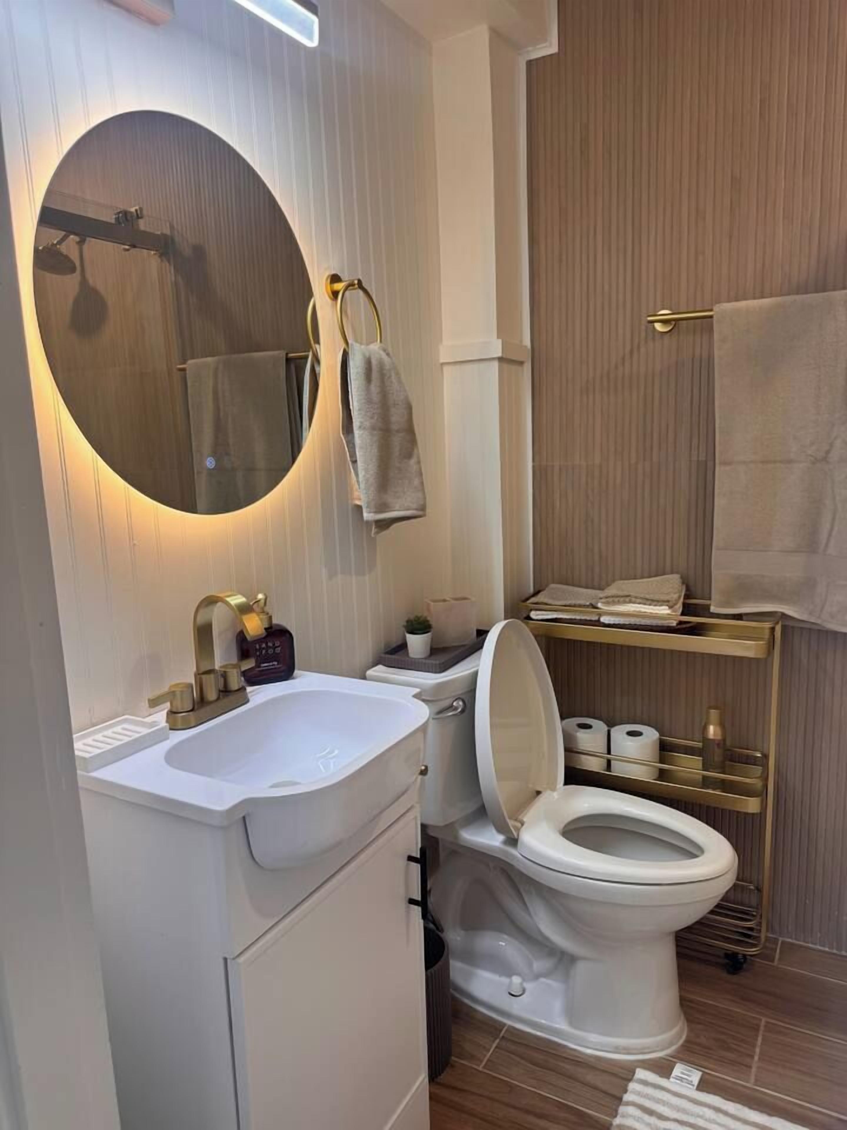 Un baño moderno con inodoro independiente, lavamanos blanco, espejo grande y un perchero para toallas.