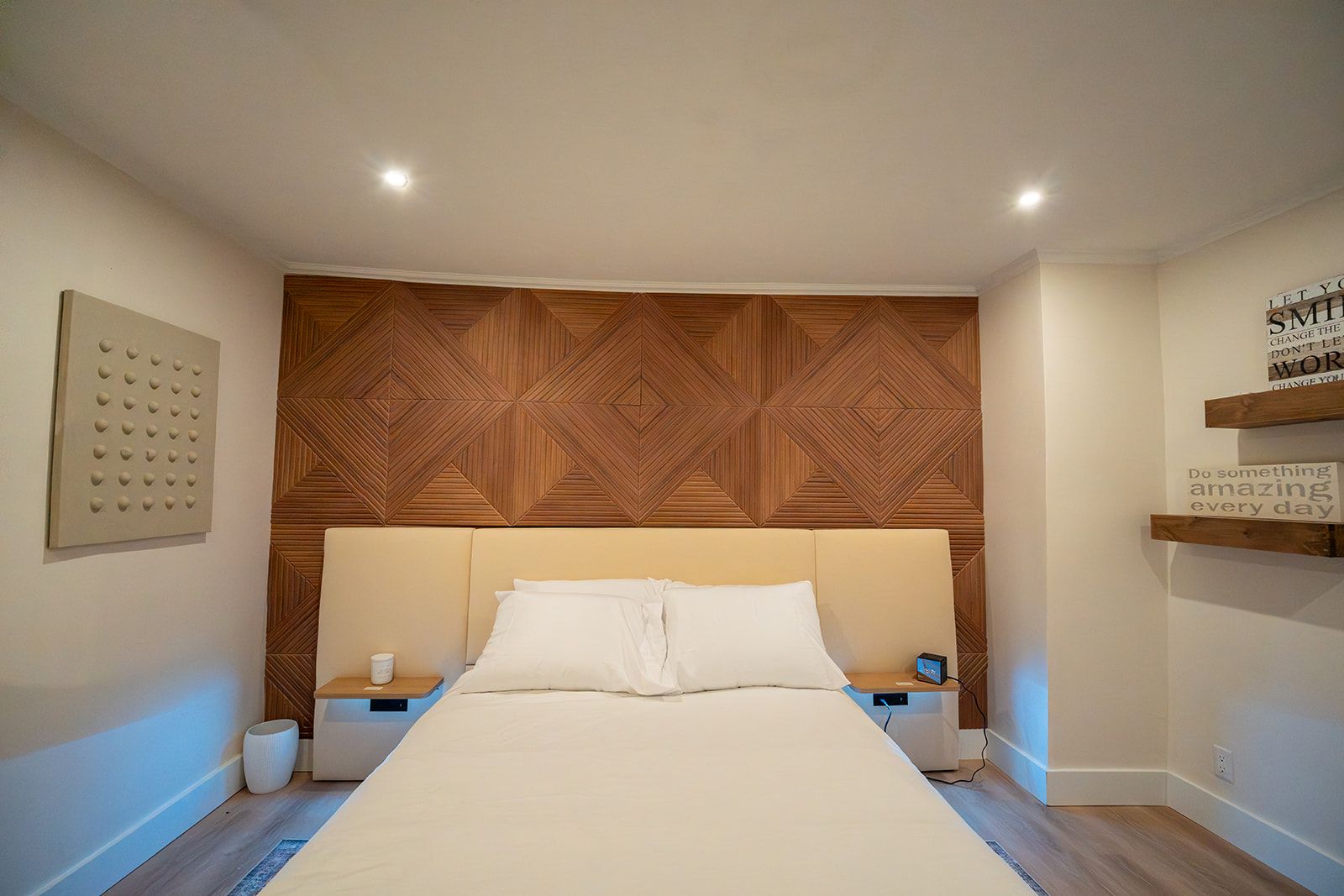 A bedroom with a large bed, wooden headboard, bedside tables, and a motivational quote on the wall.