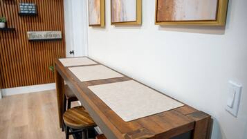 A long wooden dining table with three beige placemats, a wooden slatted wall, and a single bar stool.
