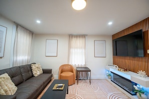 Una sala de estar moderna con un sofá, un sillón, una mesa de centro y un televisor de pantalla plana montado en una pared de madera.