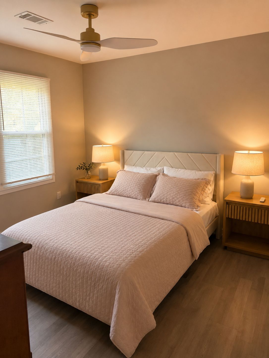 Un dormitorio con una cama, dos mesitas de noche con lámparas, un ventilador de techo y una ventana con persianas.
