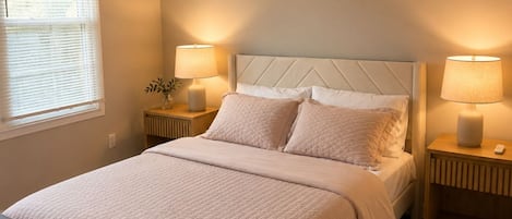 Un dormitorio con una cama, dos mesitas de noche con lámparas, un ventilador de techo y una ventana con persianas.