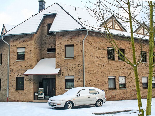 A two-story brick building with a snow-covered roof and a parked car in front.