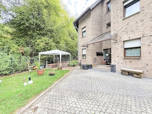 A brick building with a paved patio, a white tent, and a garden with potted plants.