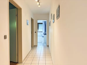 A hallway with a tiled floor, a door on the left, and a window with curtains on the right.