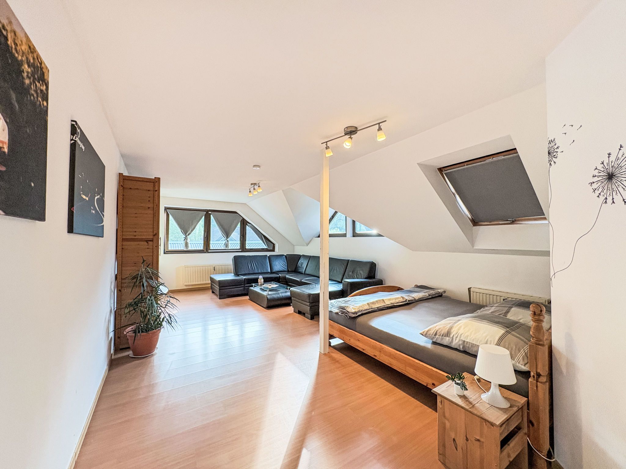 A modern loft bedroom with a large bed, a seating area with a sofa and coffee table, and a skylight.