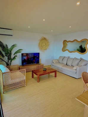Ein Wohnzimmer mit Fernseher, einer Couch, einem Couchtisch und Korbmöbeln.