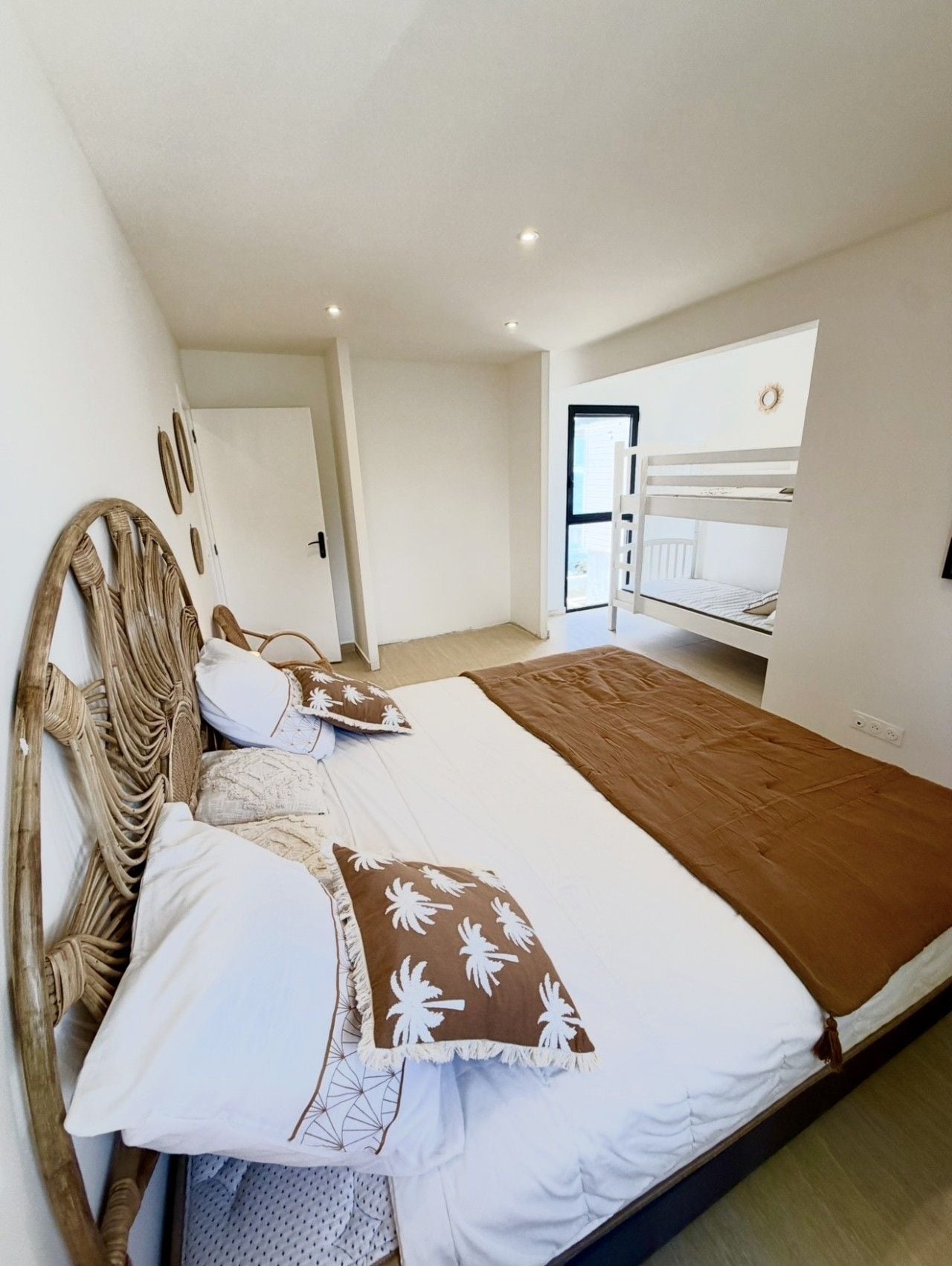 A bedroom with a bunk bed, a large bed with multiple pillows, a wooden headboard, and a window with a view.