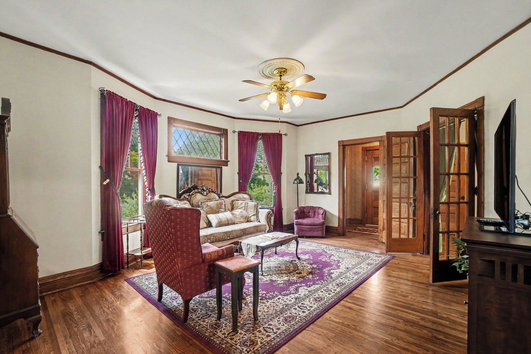 A room with a ceiling fan, a sofa, a chair, a coffee table, and a television.