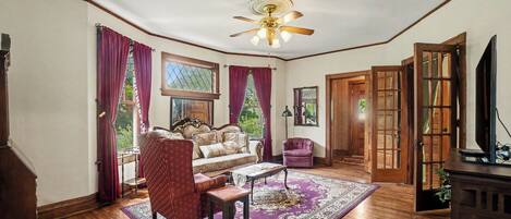A room with a ceiling fan, a sofa, a chair, a coffee table, and a television.