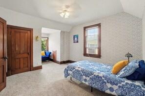 Une chambre à coucher avec un lit, une fenêtre avec des stores, une porte et un ventilateur de plafond.
