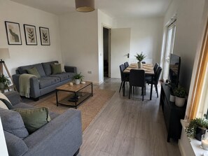 A modern living room with a grey sofa, a coffee table, and a dining area with a table and chairs. - Dartford House for Large Groups Near Bluewater (Dartford)