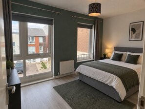 A bedroom with a large bed, two windows, a radiator, and a view of a building outside. - Dartford House for Large Groups Near Bluewater (Dartford)