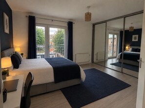 A modern bedroom with a bed, desk, chair, and a view of the outside through a sliding door. - Dartford House for Large Groups Near Bluewater (Dartford)