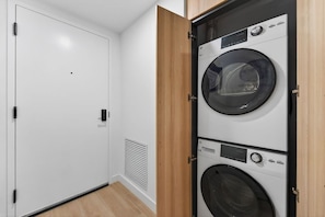 A laundry room with stacked washers and dryers, a white door, and a vent on the wall. - Elite Studio City Escape (Miami)