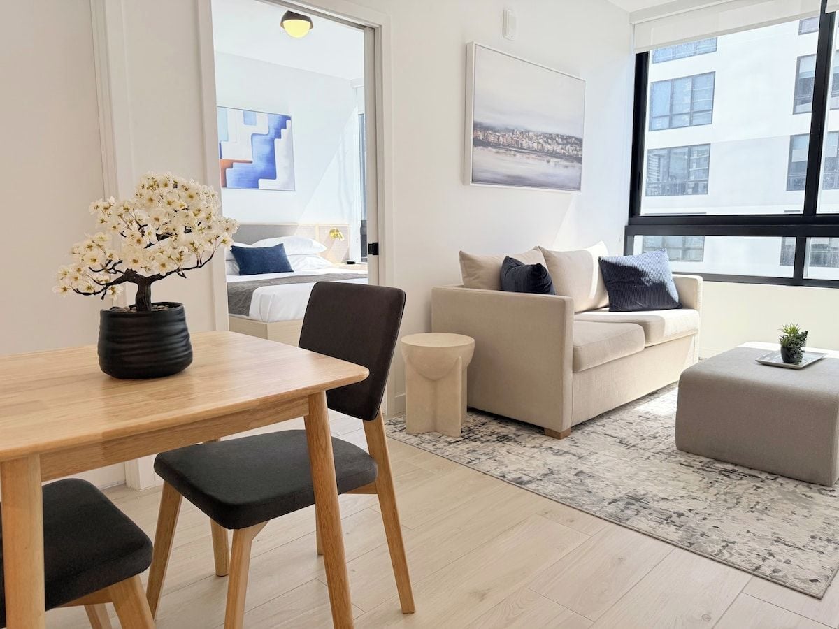 Un salon moderne comprenant un coin repas, un ensemble de canapés et une vue sur la ville grâce à de grandes fenêtres.