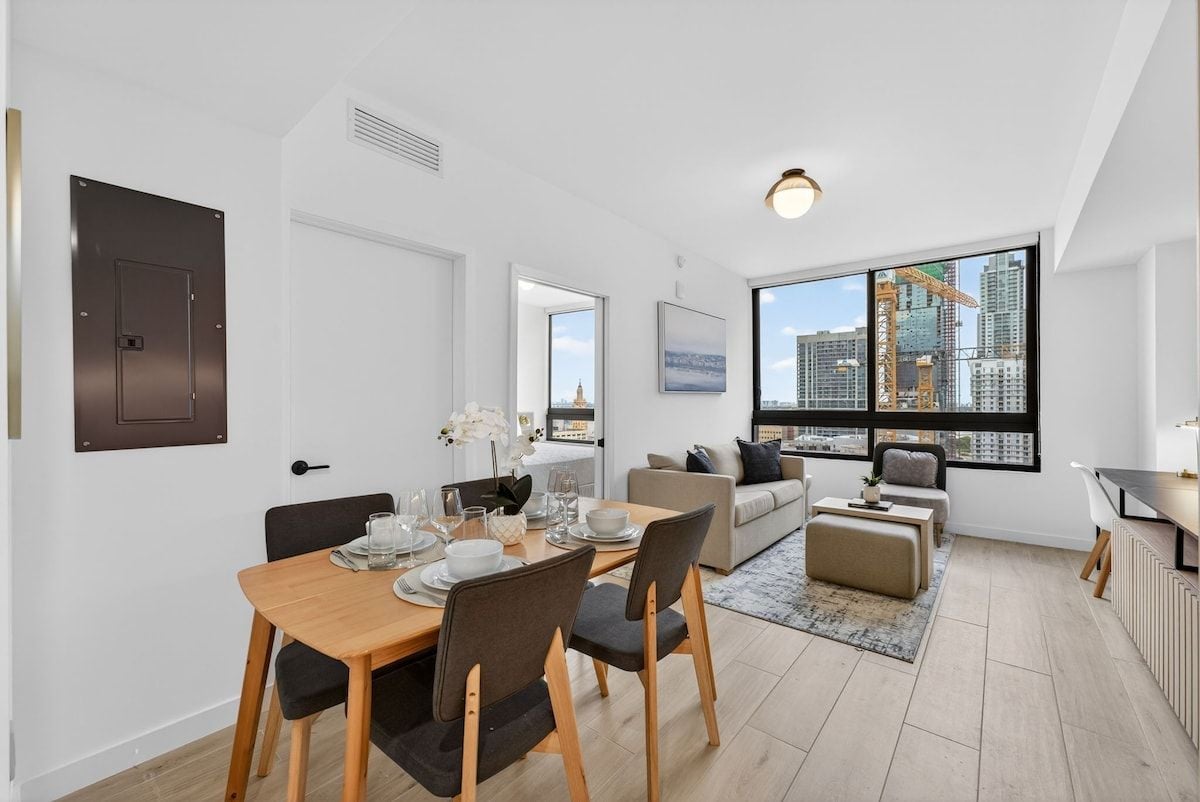 Een modern appartement met een eethoek, een woonkamer met een bank en een salontafel, en uitzicht op een stadsgezicht door grote ramen.