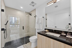 A modern bathroom with a glass-enclosed shower, a toilet, a sink with a black countertop, and a mirror. - Downtown Miami Luxe 1BR! (Miami)