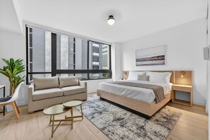 A modern bedroom with a large bed, a sofa, a small table, and a potted plant. - Modern Luxe Downtown Stay (Miami)