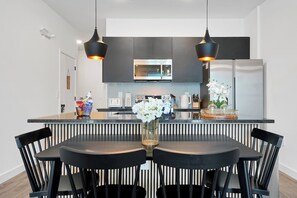 A modern kitchen with a central island, black chairs, and a vase of flowers. - Magical Family Getaway (Kissimmee)