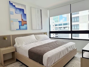 A modern hotel room with a large bed, a bedside table, a window with a city view, and abstract art on the wall. - Chic Luxury 1BR Oasis (Miami)