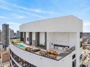 Um edifício moderno com terraço no telhado, que inclui piscina, área de estar ao ar livre e guarda-corpo de vidro.