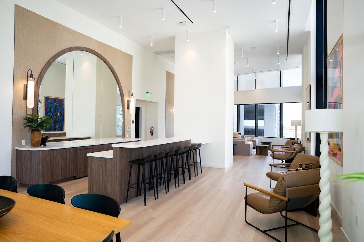 Een moderne hotel lobby met een centrale bar, zithoek en een grote spiegel.