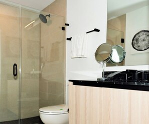 Un bagno moderno con cabina doccia in vetro, un water, un lavabo con piano in nero e uno specchio.