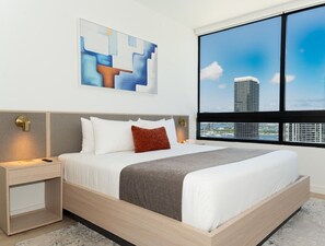 Ein modernes Hotelzimmer mit einem großen Bett, einem Nachttisch, einem Gemälde und Blick auf die Stadt.