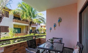 A balcony with wicker furniture, a glass table, and a view of palm trees and a building. - Ground Floor Apt. w/ Balcony & Pool Bvd0003 (Porto Seguro)