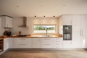 A modern kitchen with white cabinets, a large window, and a view of the outdoors. - Villa Casa com Alma – Douro with Private Pool, Wi-Fi and Air Conditioning (Peso da Régua)