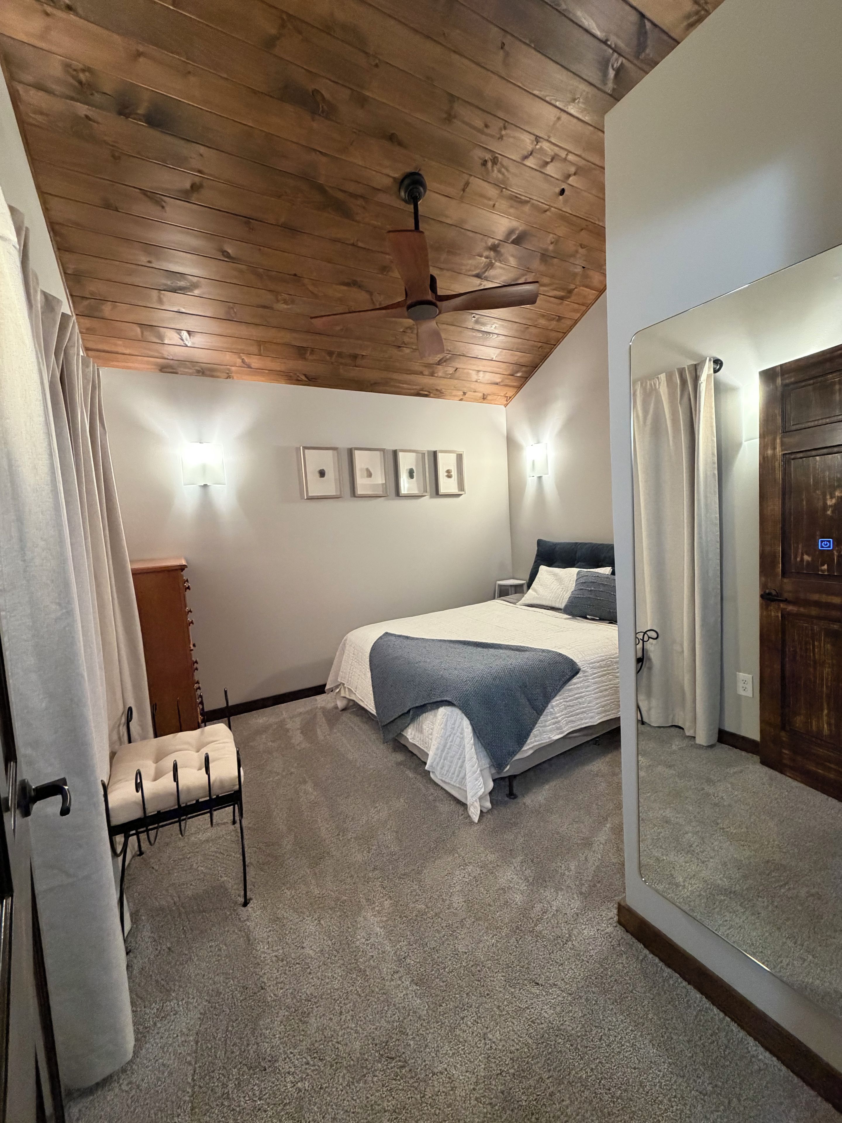 Een slaapkamer met een bed, een plafondventilator, een lamp en een spiegel.