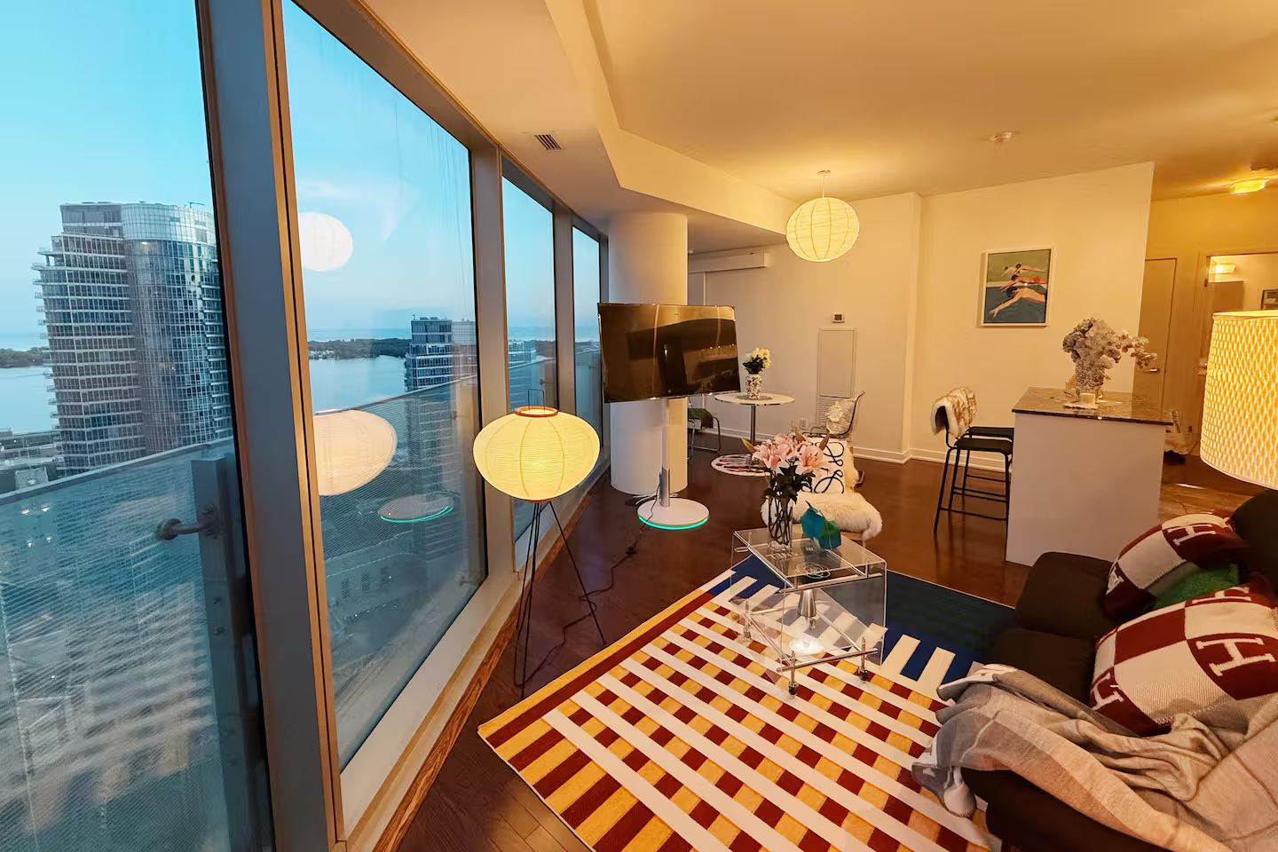 Ein modernes Wohnzimmer mit einem großen Fenster, einem karierten Teppich und Blick auf eine Stadtlandschaft.