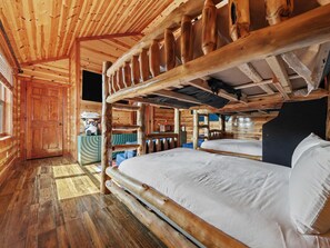 Ein rustikales Blockhaus-Interieur mit Holzbalkendecke, einem zentral platzierten Bett mit Kopfteil und einer kleinen Küchenzeile.