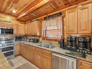 A kitchen with wooden cabinets, a stainless steel oven, a coffee station, and a fire safety sign. - Smoky Mtn Views | Indoor Pool, Hot Tub & Sauna (Sevierville)