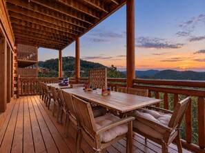 Eine Holzterrasse mit Tisch und Stühlen, mit Blick auf eine Berglandschaft bei Sonnenuntergang.