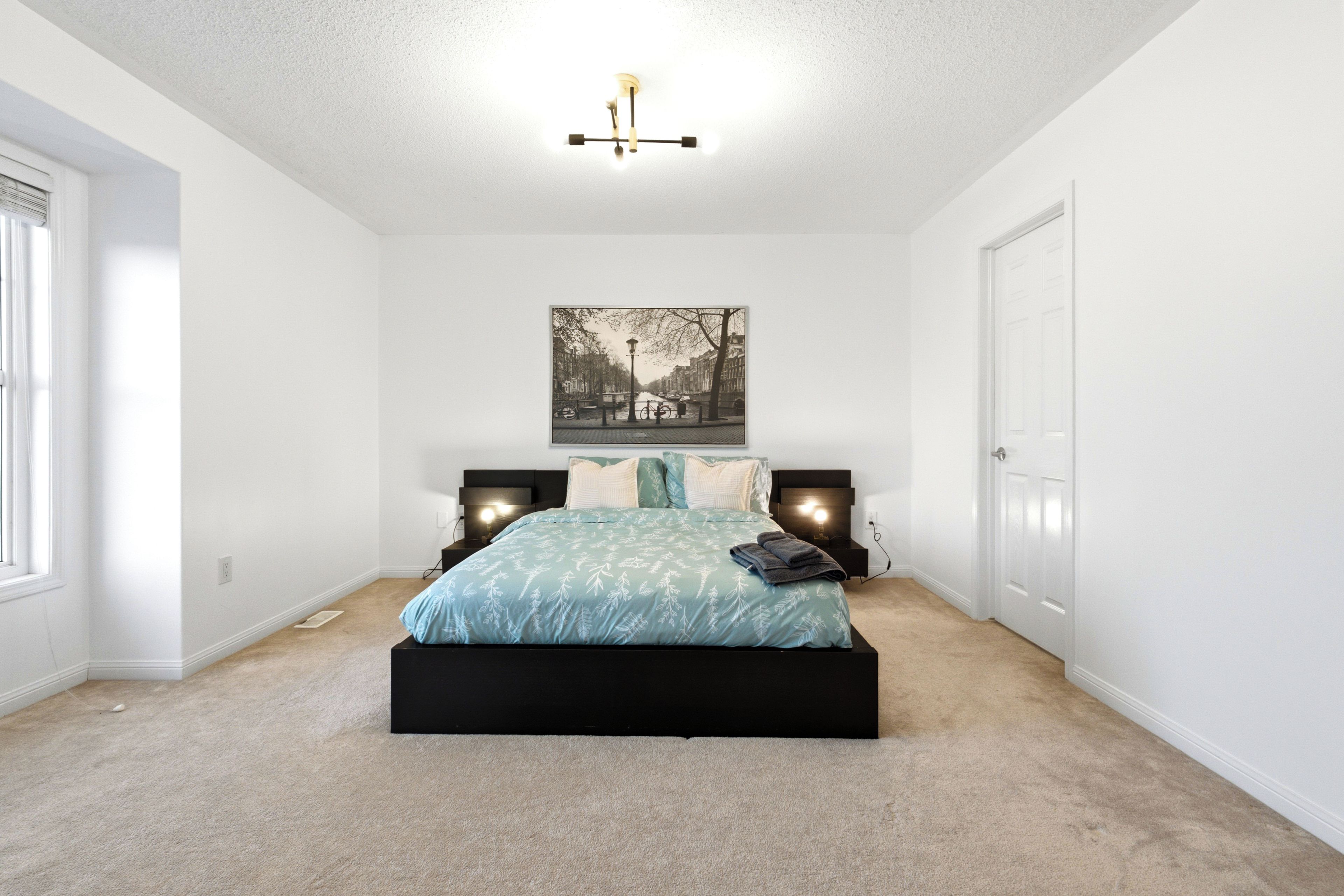 A bedroom with a bed, two bedside tables, a wall-mounted light fixture, and a framed picture on the wall.