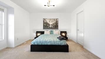 A bedroom with a bed, two bedside tables, a wall-mounted light fixture, and a framed picture on the wall.