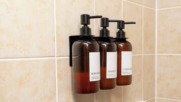 Three bottles of body wash and shampoo on a wall-mounted dispenser in a bathroom.