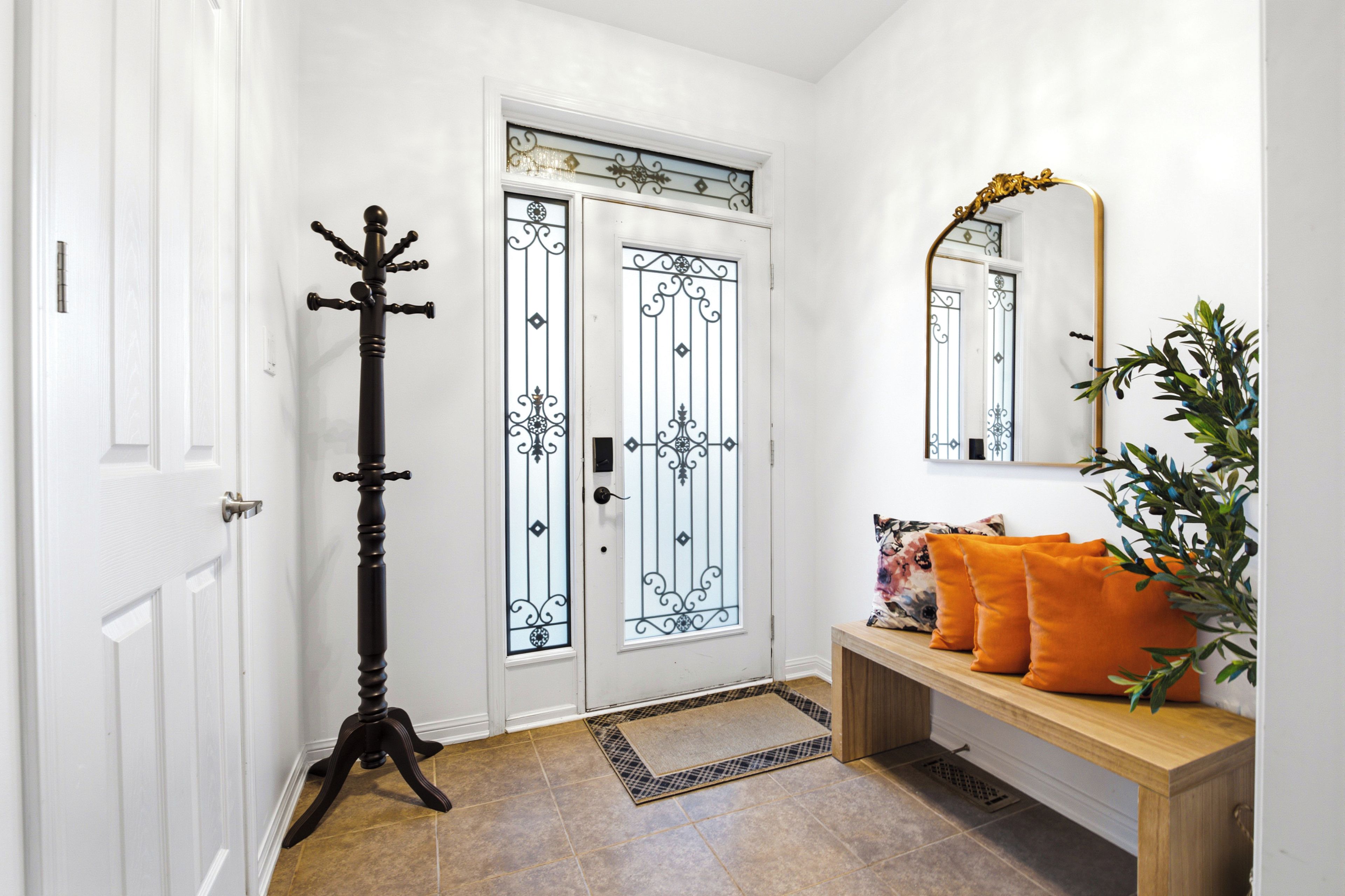 Un couloir avec une porte blanche, un porte-manteau, un banc avec des coussins et un miroir au mur.
