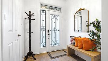Un couloir avec une porte blanche, un porte-manteau, un banc avec des coussins et un miroir au mur.