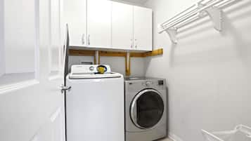 Une buanderie équipée d’un lave-linge et d’un sèche-linge, avec des armoires blanches et un étendoir.