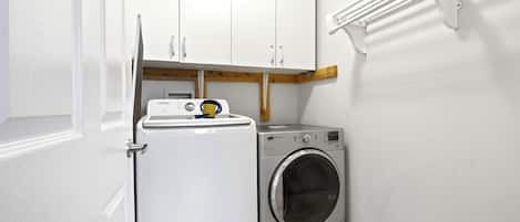 A laundry room with a washing machine and dryer, white cabinets, and a drying rack.
