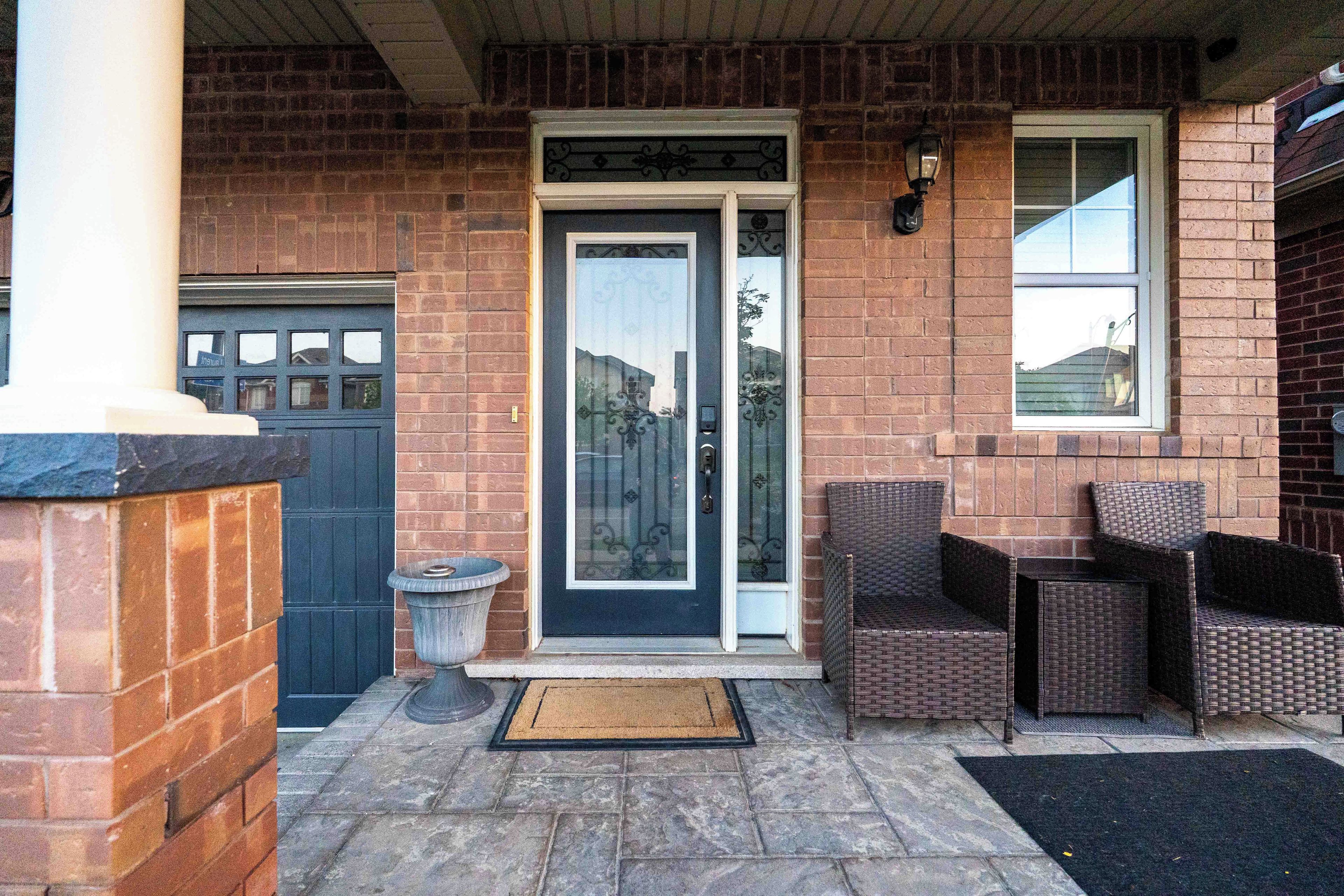 A brick building with a dark blue door, a small garden area with wicker furniture, and a visible garage door.