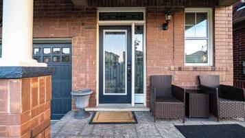 A brick building with a dark blue door, a small garden area with wicker furniture, and a visible garage door.
