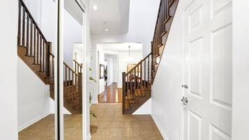 Un pasillo con una escalera de madera que lleva a una plataforma, paredes blancas y piso de baldosas.