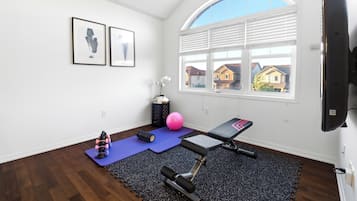 A room with a large window, a treadmill, a yoga mat, and a wall-mounted TV.