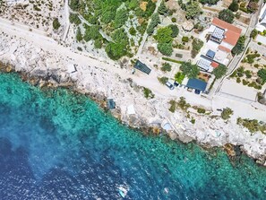 Luftaufnahme eines Küsteneigentums mit felsiger Küstenlinie, klarem türkisblauem Wasser und einer Mischung aus Wohn- und Geschäftsgebäuden.
