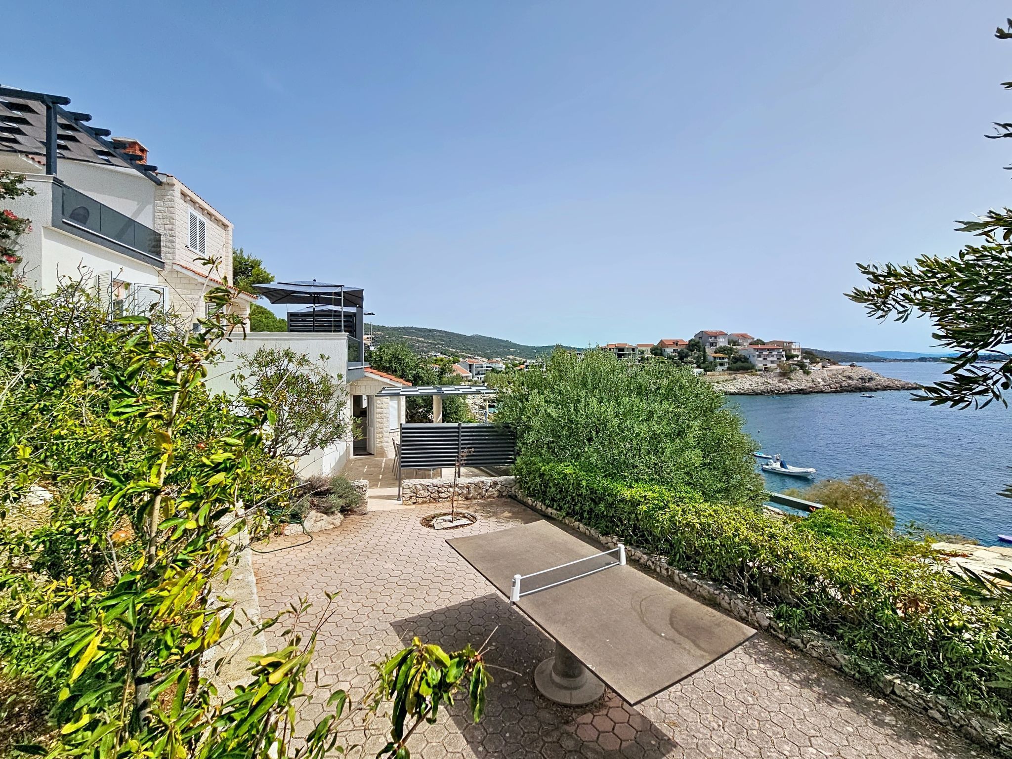 A residential area with a paved patio, a view of the sea, and a hillside with buildings.