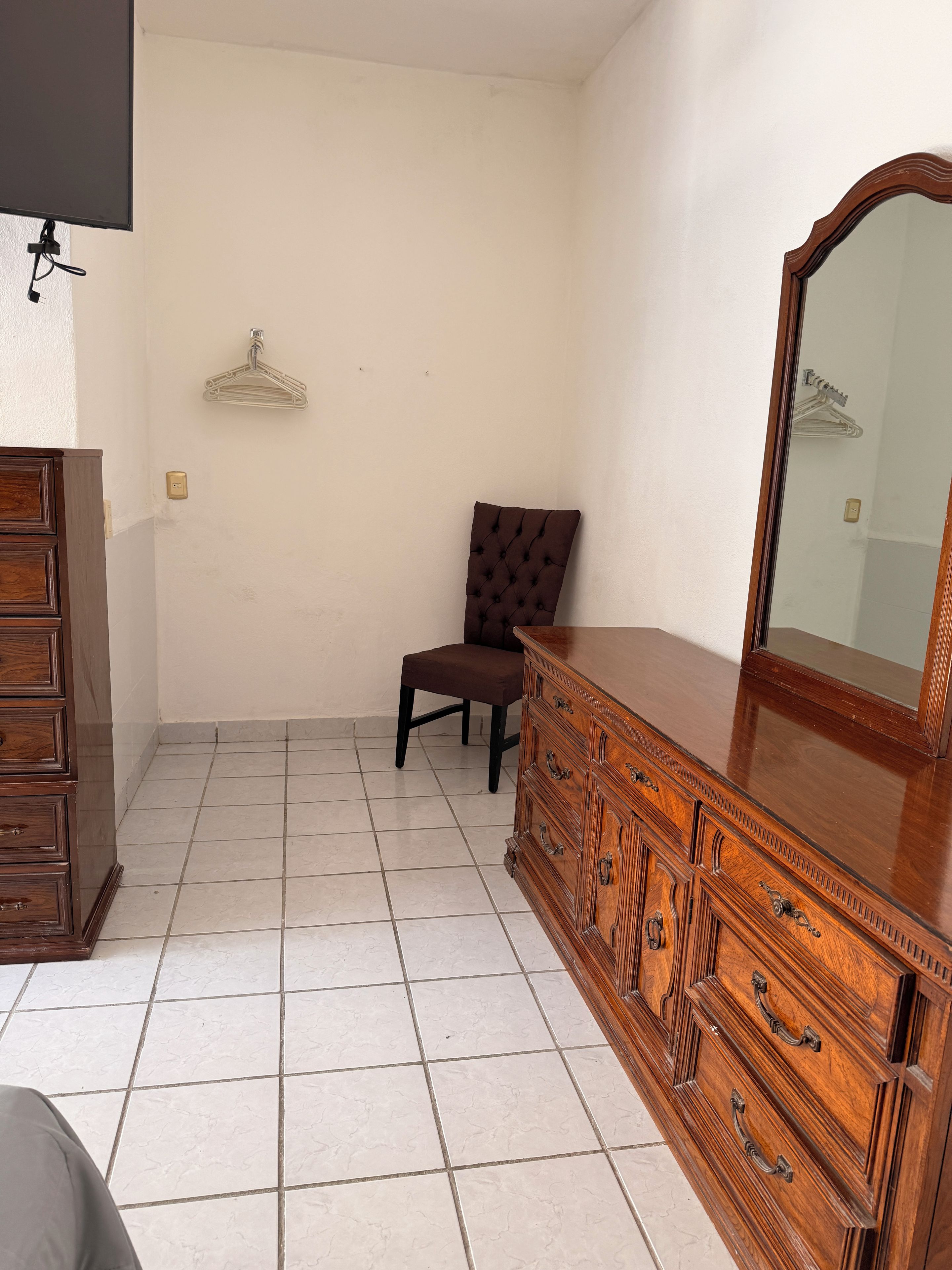 A room with a wooden dresser, a chair, and a mirror.